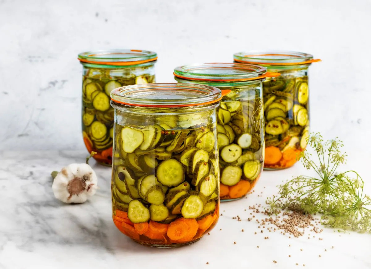 Słoiki z ogórkami i marchewką, idealne do przygotowania sałatki szwedzkiej. Obok czosnek i koperek.