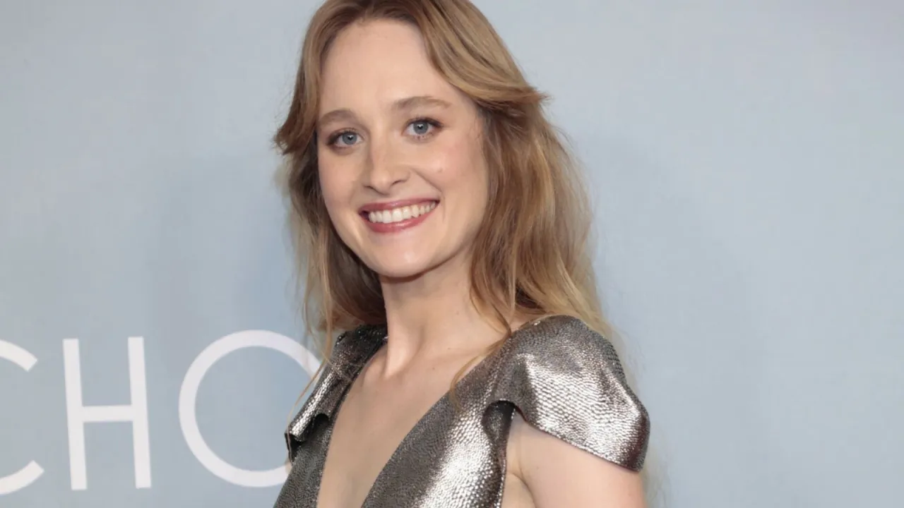 Uśmiechnięta Maria Kowalska, aktorka, w błyszczącej sukni z falbankami na ramionach.