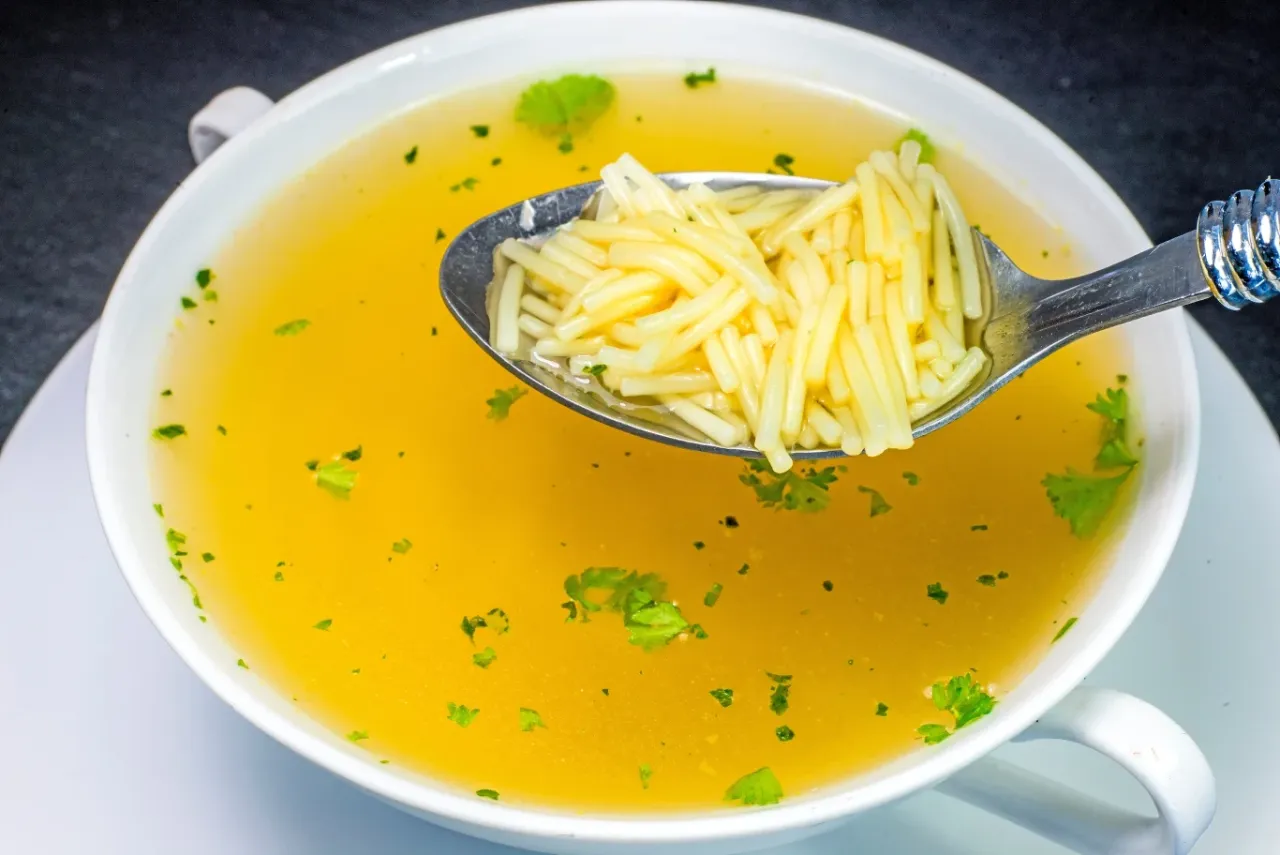 Kucharz usuwający szumowiny łyżką cedzakową