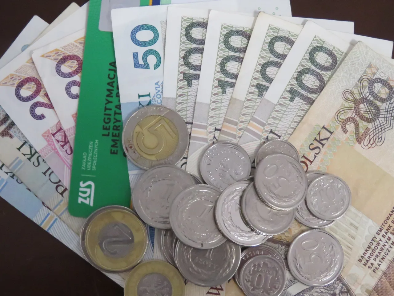 ZUS legitymacja emeryta i monety obok banknotów 20, 50, 100, 200 zł. Ile wynosi trzynasta emerytura netto?