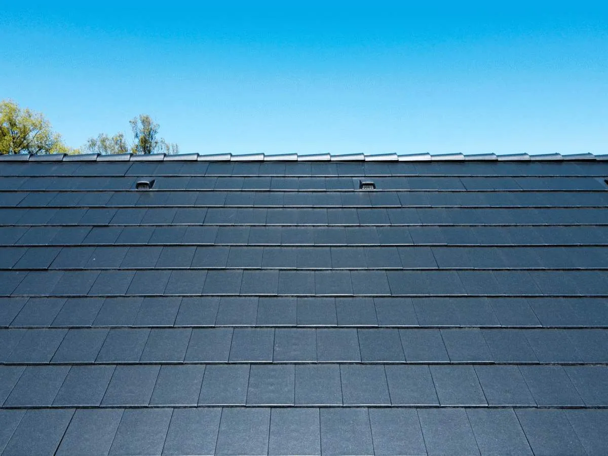 Ciemnoszara dachówka płaska ułożona prosto, tworząca równą, jednolitą powierzchnię dachu pod błękitnym niebem.
