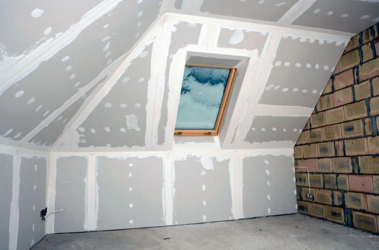 Poddasze w trakcie prac wykończeniowych, z oknem dachowym i widokiem na niebo. To etap kompleksowej termomodernizacji, kt&oacute;ra zapewni czyste powietrze i komfort.