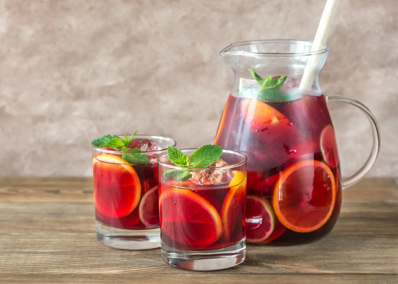 Dwa szklanki i dzbanek pełne orzeźwiającej, czerwonej sangrii z owocami i miętą. Idealny wybór na lato, czy to Sangria czerwona czy Sangria biała.