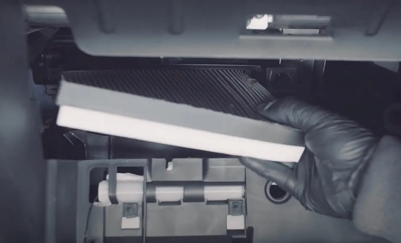 Rękawiczka w czarnej rękawiczce wyjmuje nowy filtr kabinowy, przygotowując się do jego wymiany.