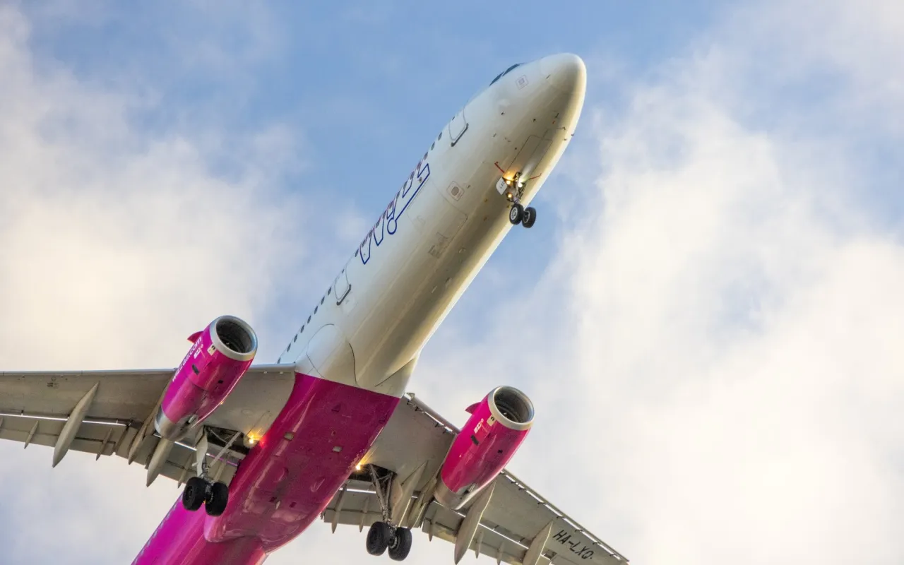 Samolot Wizzair, znane linie lotnicze, wznosi się na tle błękitnego nieba z chmurami.