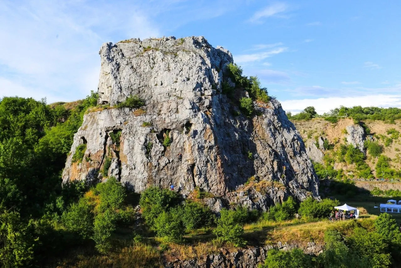 Wspinacze na skalnej ścianie w rezerwacie przyrody Kielce. W dole namioty i zielona roślinność.