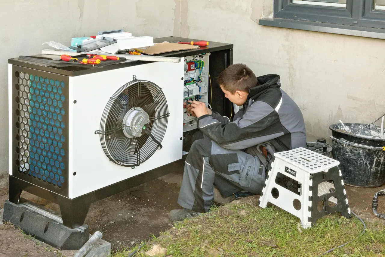 Technik pracuje przy pompie ciepła, sprawdzając jej działanie. Regularny przegląd pompy ciepła zapewnia jej sprawność.