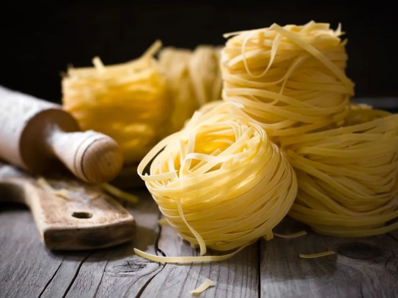 Stos suchych, żółtych tagliatelle na drewnianym blacie. Obok wałek i deska. Idealny makaron, jaki makaron jest dietetyczny?