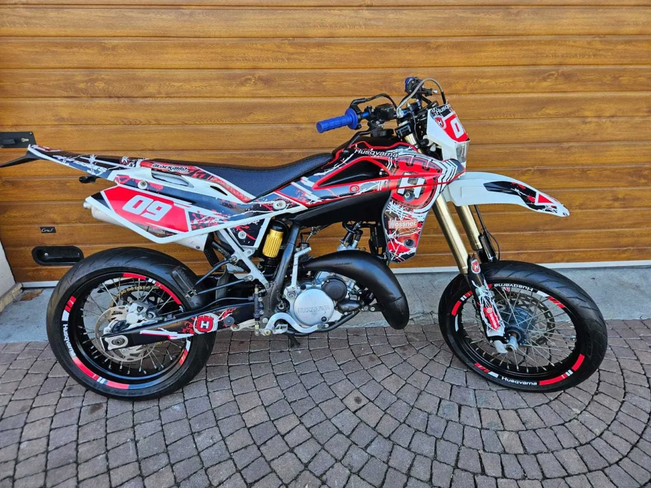 Agresywny Husqvarna 125 supermoto w czerwono-białych barwach, gotowy do akcji na torze.