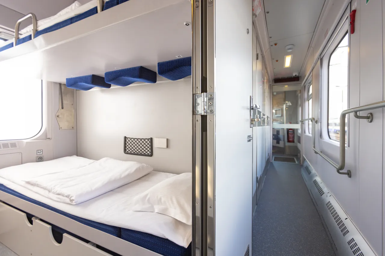 Wnętrze wagonu sypialnego z piętrowymi łóżkami i korytarzem. Zastanawiasz się, ile kosztuje wagon sypialny?