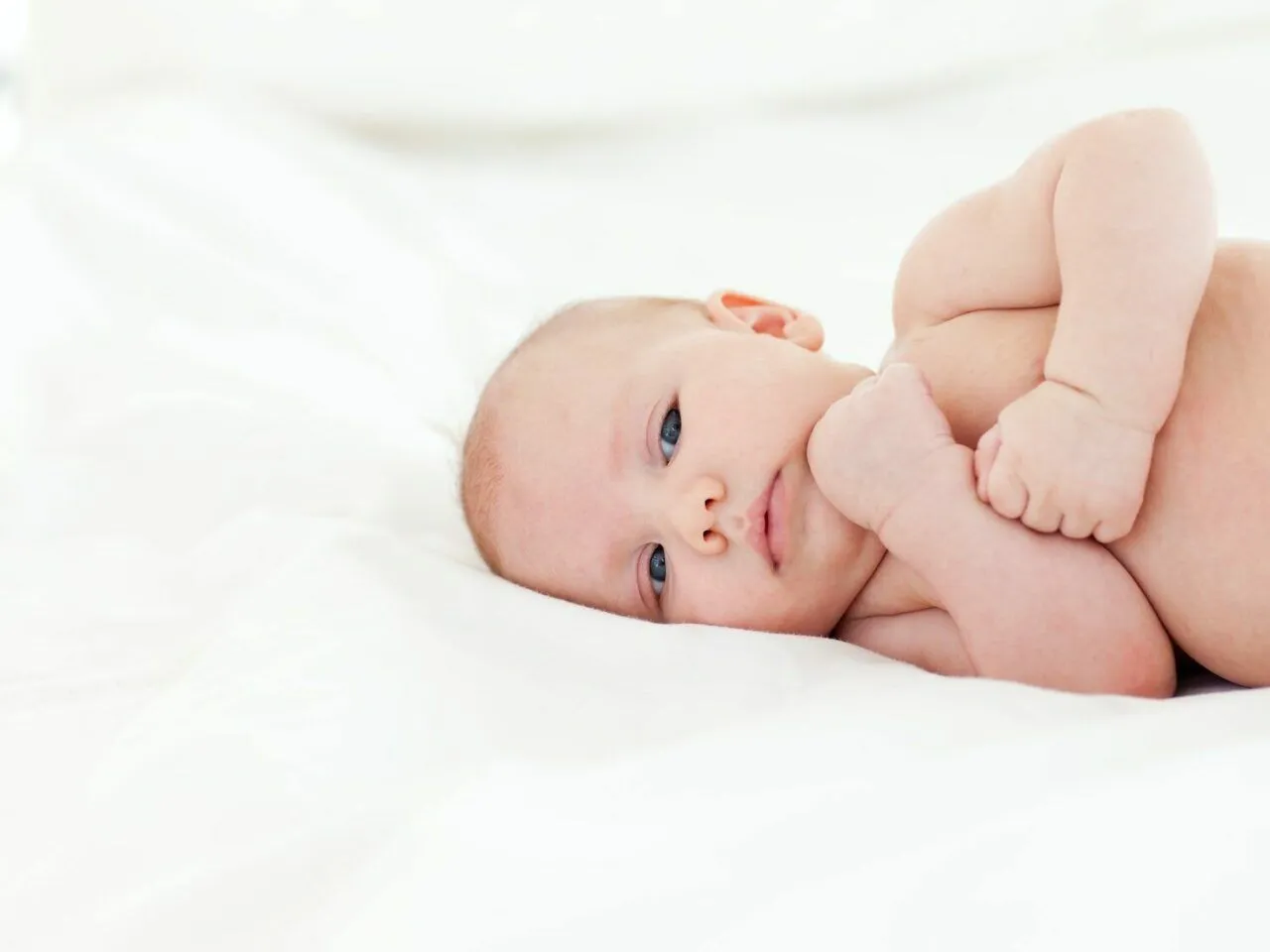 4 miesięczne dziecko bawi się grzechotką, niemowlę obraca się z plec&oacute;w na brzuszek