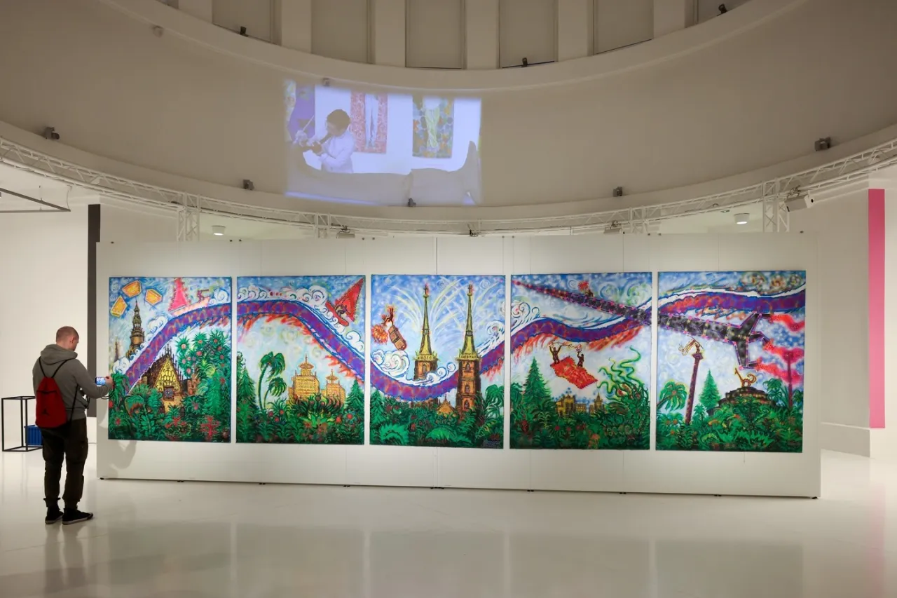 W muzeum sztuki Wrocław mężczyzna ogląda wielopanelowy obraz z fantastycznym krajobrazem i latającymi obiektami.
