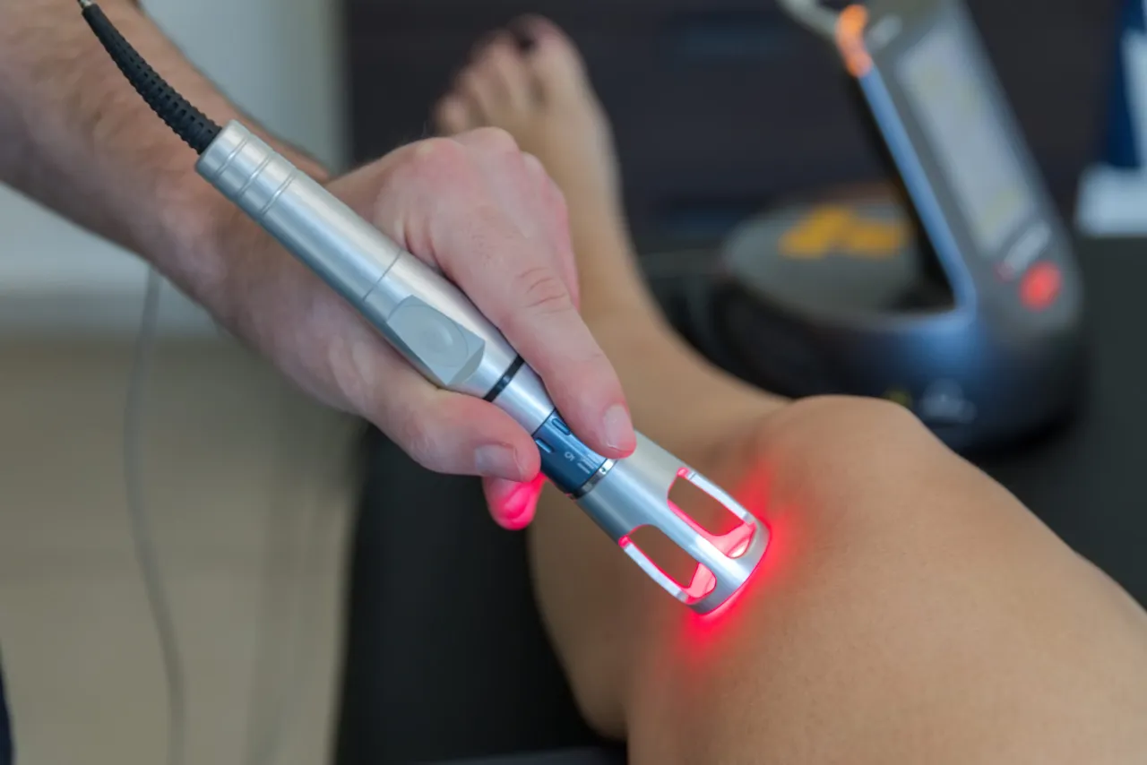 Terapeuta aplikuje laser na kolano pacjenta, pokazując, jak działa laser w rehabilitacji.