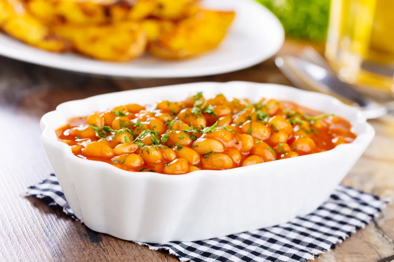 Aksamitna fasolka po bretońsku w sosie pomidorowym, posypana natką pietruszki. Obok talerz ziemniaków.