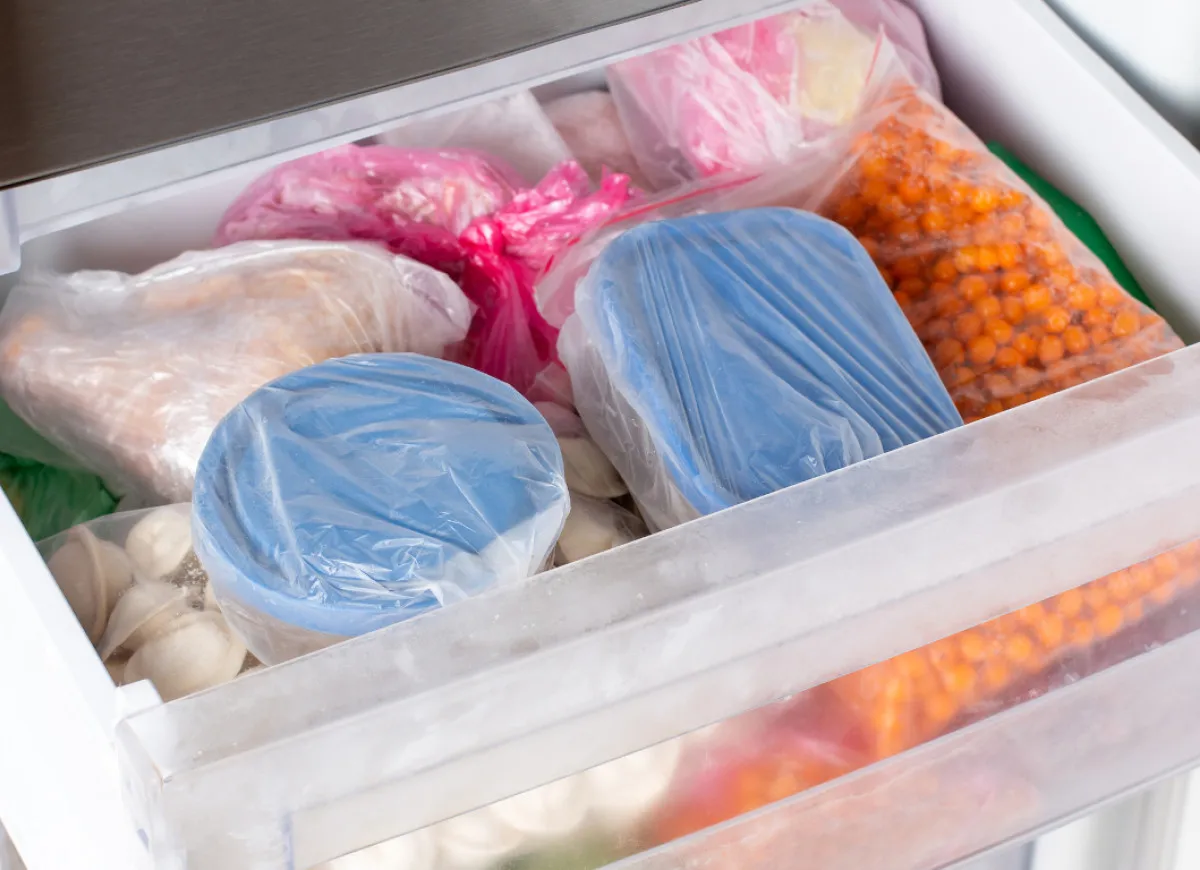 Sposoby na to, jak mrozić zupy: pojemniki z niebieskimi pokrywkami, woreczki z mięsem, pierożkami i owocami morza w zamrażarce.
