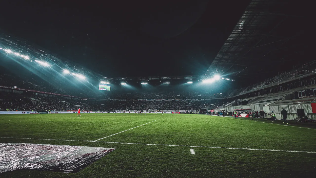 Nocny mecz na stadionie, rozświetlonym jupiterami. Kibice na trybunach czekają, kiedy terminarz ekstraklasy przyniesie kolejne emocje.