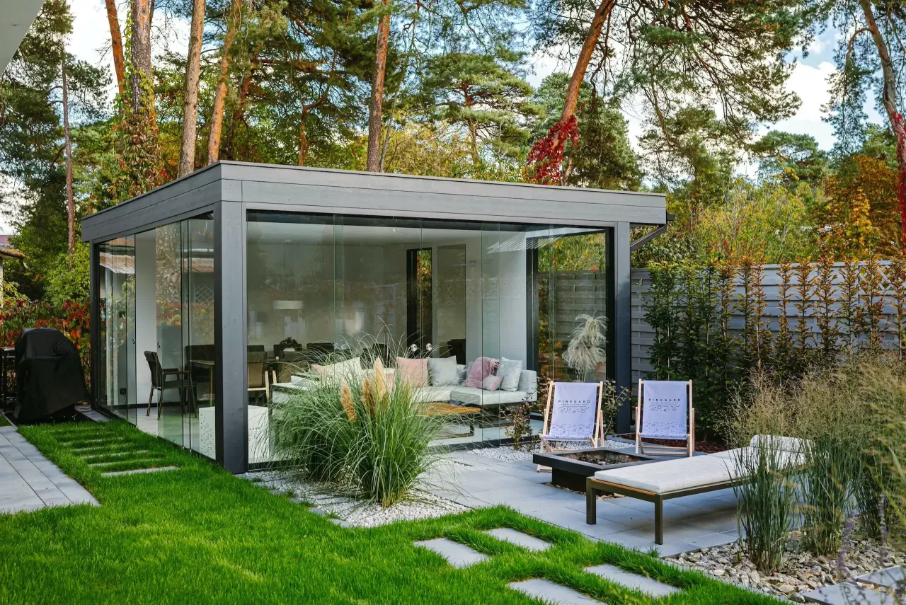 Nowoczesna altana ze szklanymi ścianami, idealna na relaks. Na dachu altany rosną drzewa, tworząc naturalny cień.