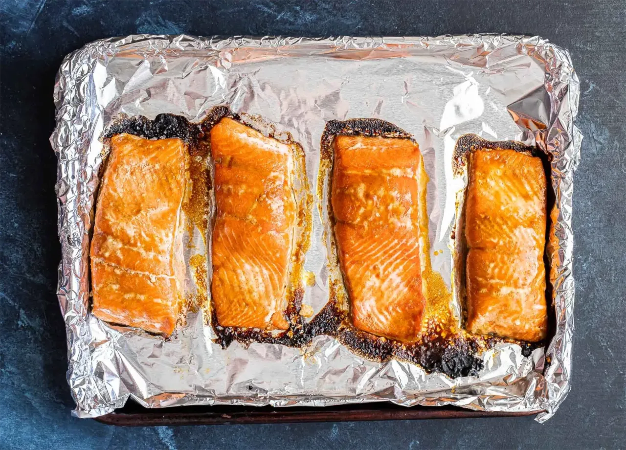 Cztery kawałki łososia pieczone na folii aluminiowej, gotowe do przygotowania sushi.