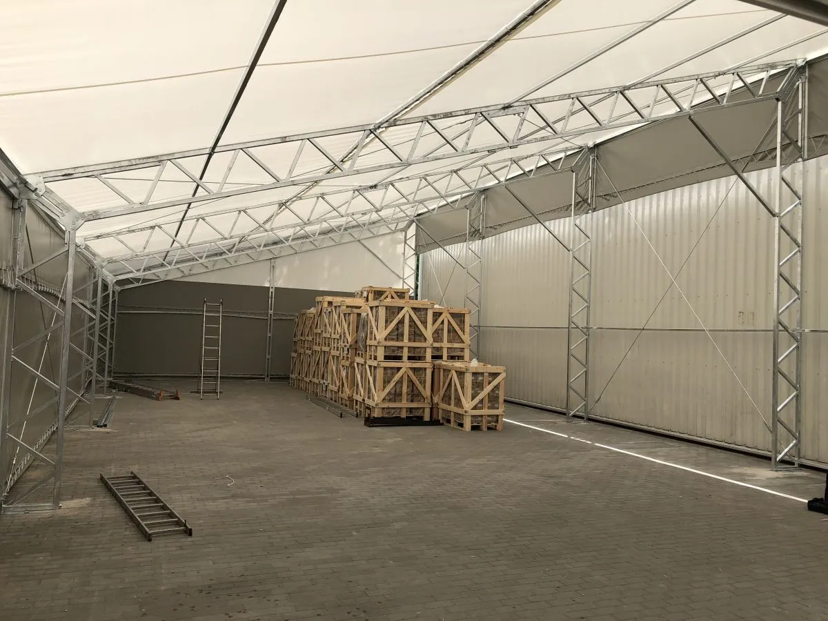 Wnętrze hali magazynowej z drewnianymi skrzyniami. Czy postawienie namiotu magazynowego wymaga pozwolenia na budowę?