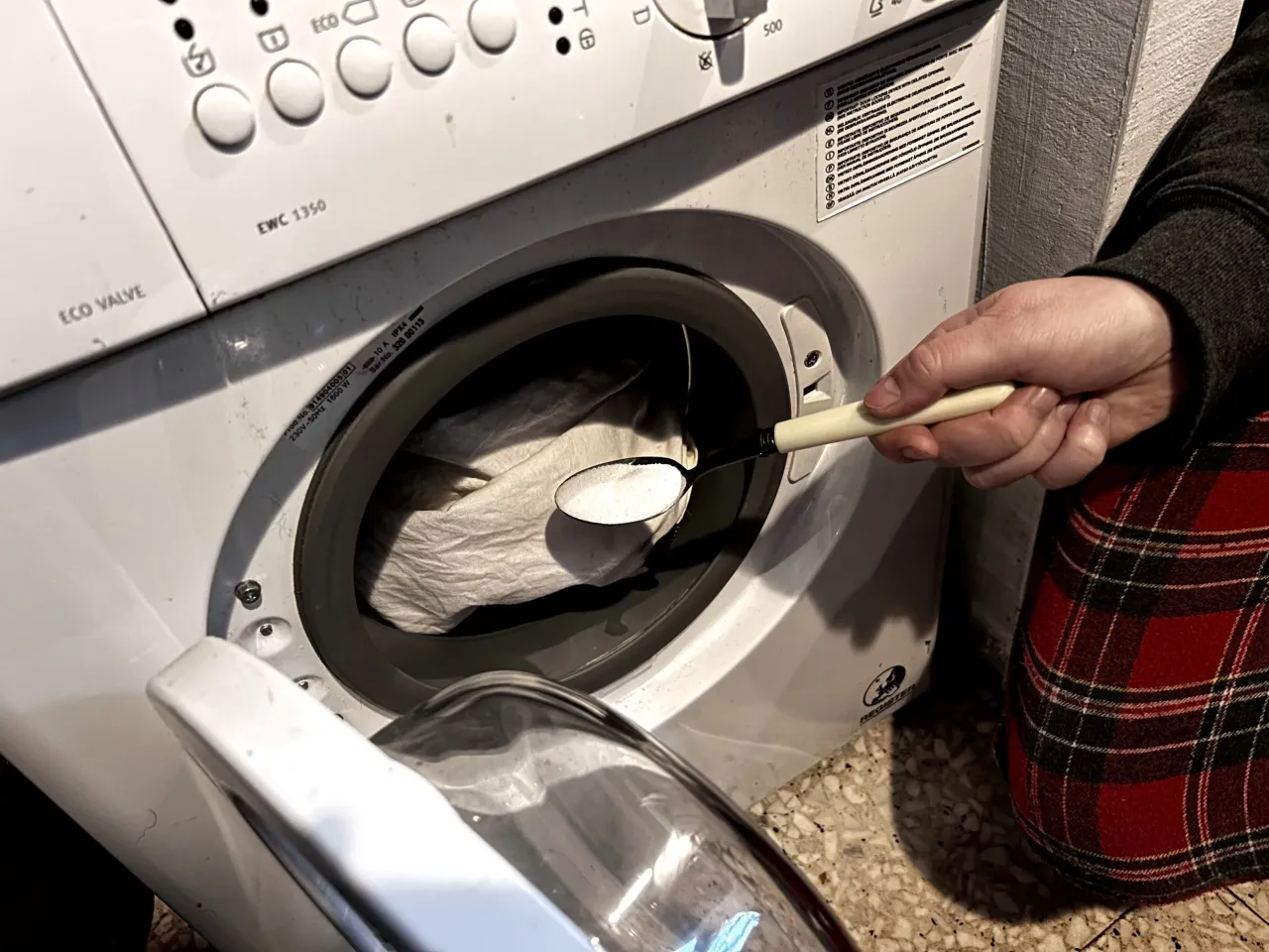 butelka odplamiacza obok butelki wybielacza na tle pralki