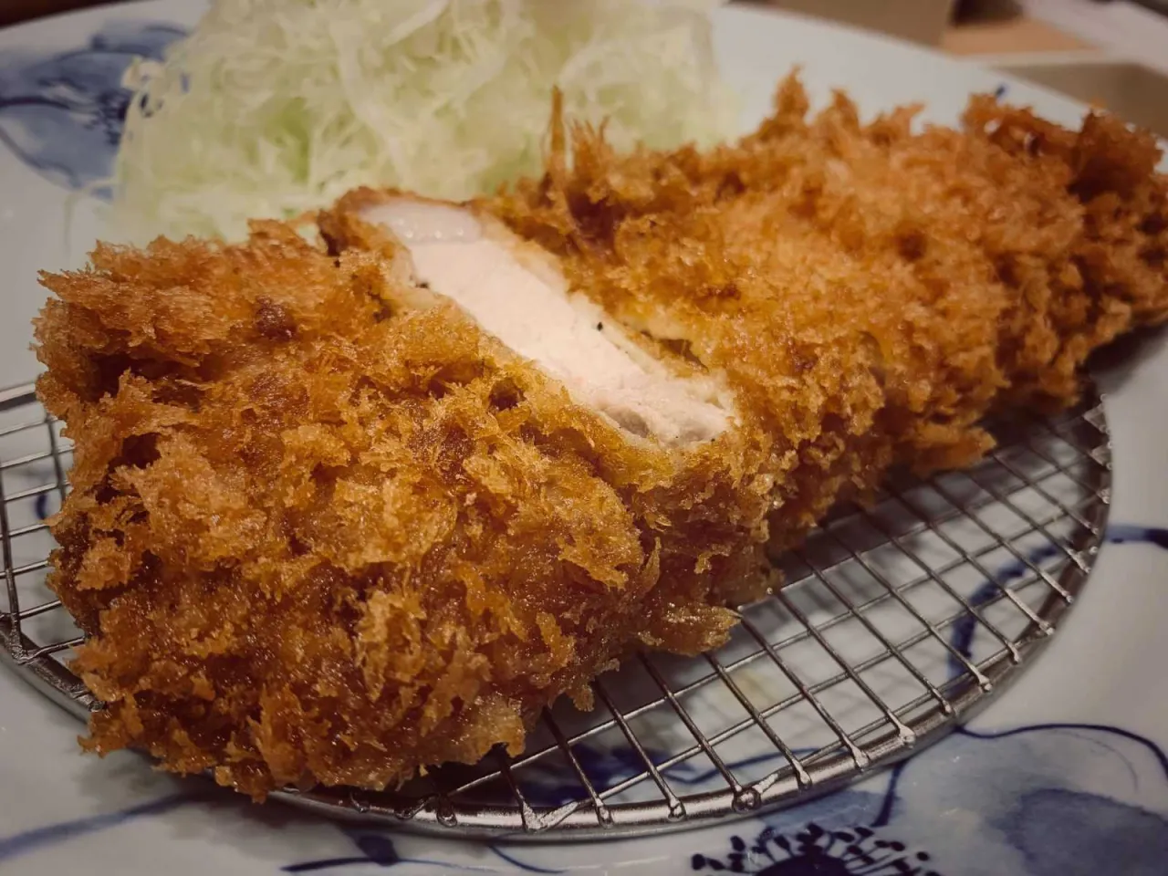 Chrupiący schabowy w panko, soczysty w środku, podany z poszatkowaną kapustą na talerzu z niebieskimi wzorami.