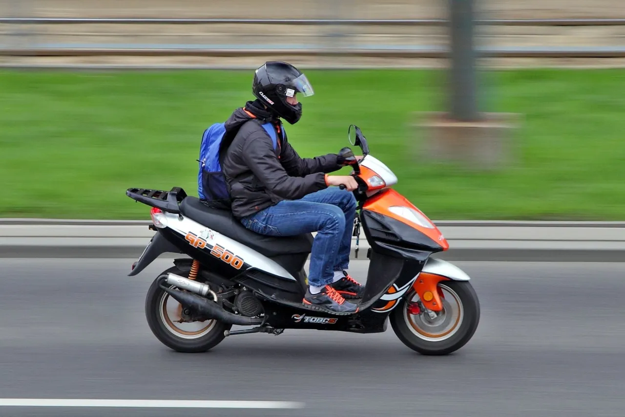 Młody mężczyzna w kasku jedzie skuterem GP-500. To jeden z tych pojazdów, jakim motorem można jeździć bez prawa jazdy, idealny do miejskich podróży.