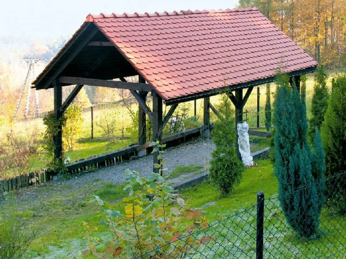 Solidne wiaty garażowe drewniane z czerwonym dachem, otoczone zielenią i jesiennym krajobrazem.