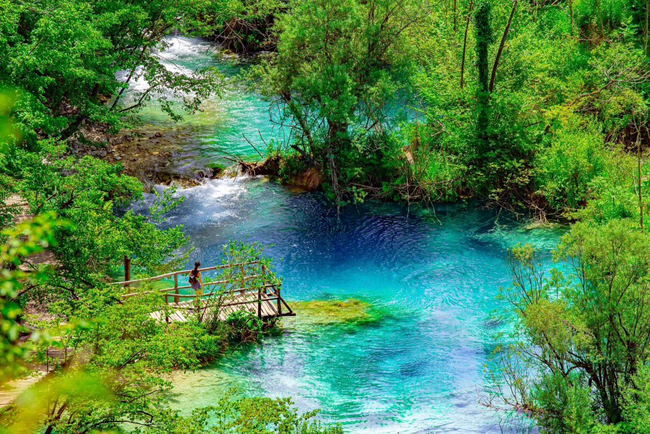 Turkusowa woda i bujna zieleń &ndash; to chorwacja najpiękniejsze miejsca. Kobieta na drewnianej kładce podziwia widok.