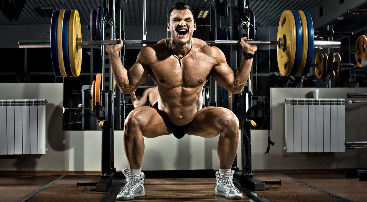 Osoba ćwicząca przysiady ze sztangą na siłowni