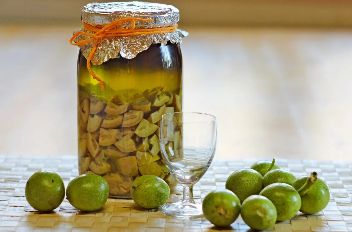 Nalewka z niedojrzałych orzechów włoskich, które najlepiej zbierać w czerwcu. Obok słoika stoi kieliszek.