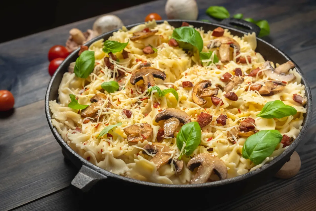 Pyszne farfalle z grzybami i boczkiem, posypane parmezanem i bazylią. Idealny pomysł, co można zrobić z ugotowanym makaronem na szybki obiad.