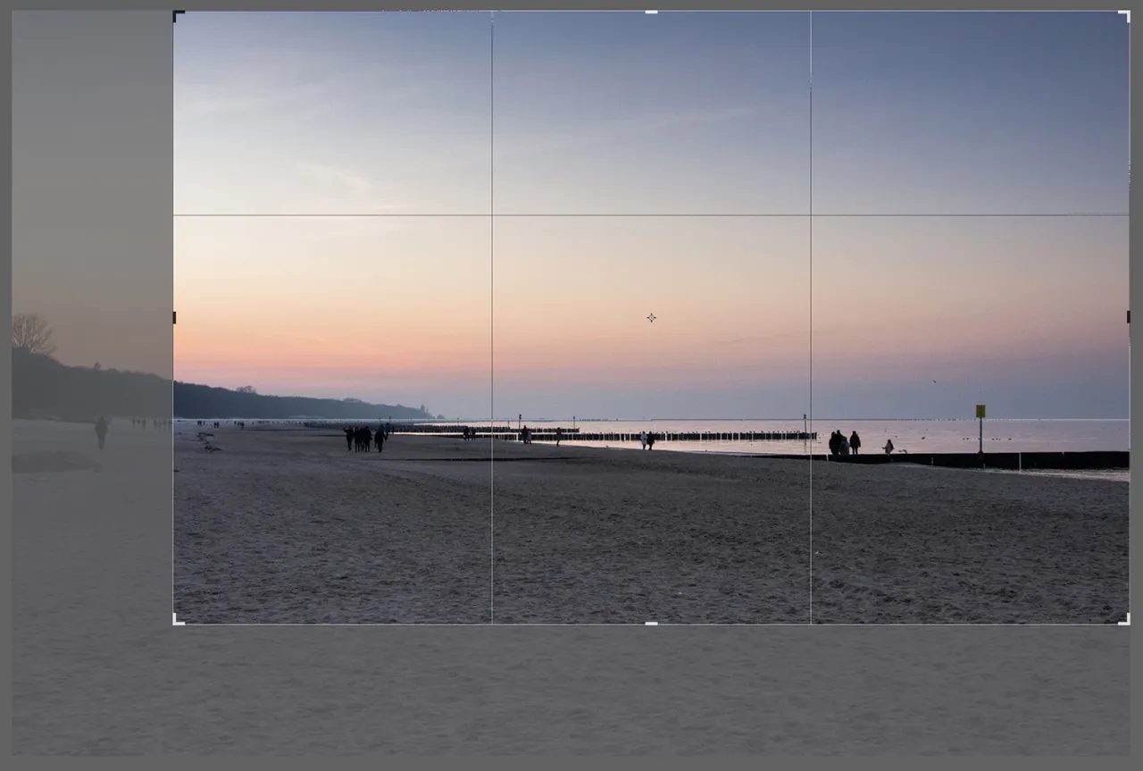 Zach&oacute;d słońca na plaży, z widocznymi ludźmi spacerującymi po piasku. Idealny moment, by nauczyć się, jak wyprostować zdjęcie w Photoshopie.