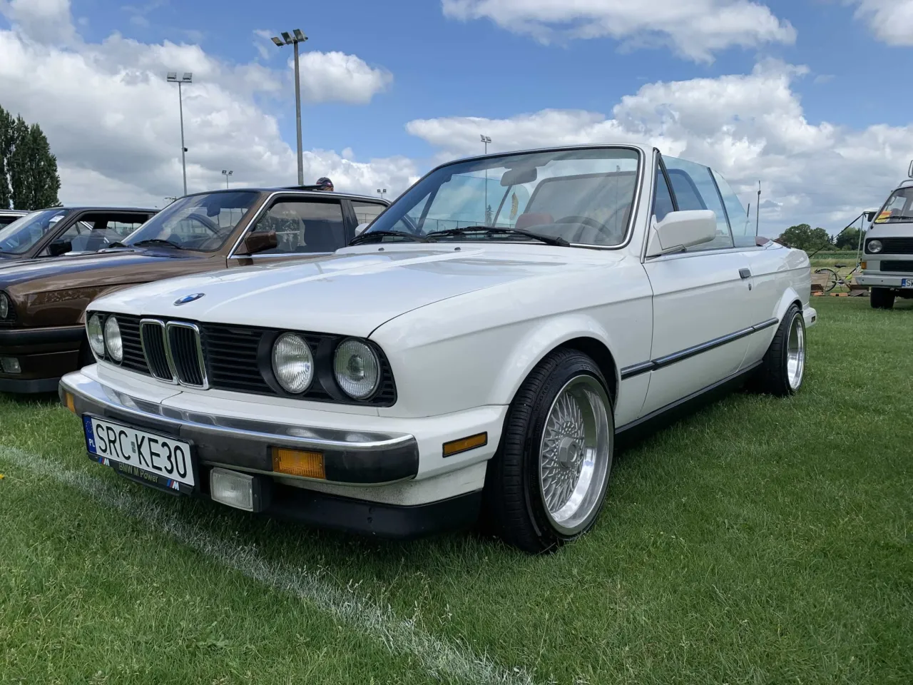 Białe bmw e30 cabrio z chromowanymi felgami stoi na trawie.
