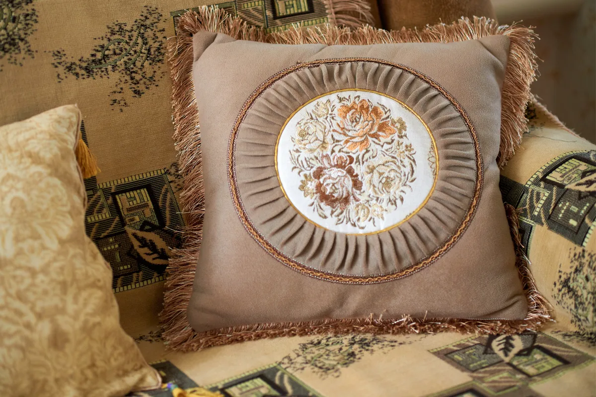 Brązowa poduszka z haftem kwiatowym, ozdobiona frędzlami. Idealna do stworzenia własnej makramy poduszki krok po kroku.