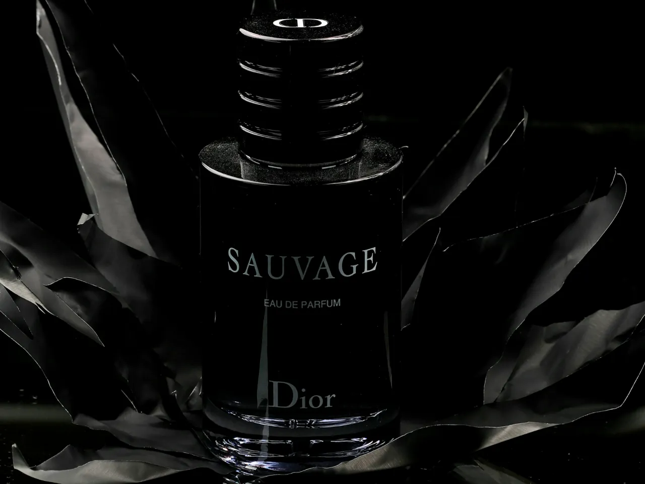 Elegancka woda perfumowana Dior Sauvage dla mężczyzn, otoczona czarnymi, falującymi płatkami.