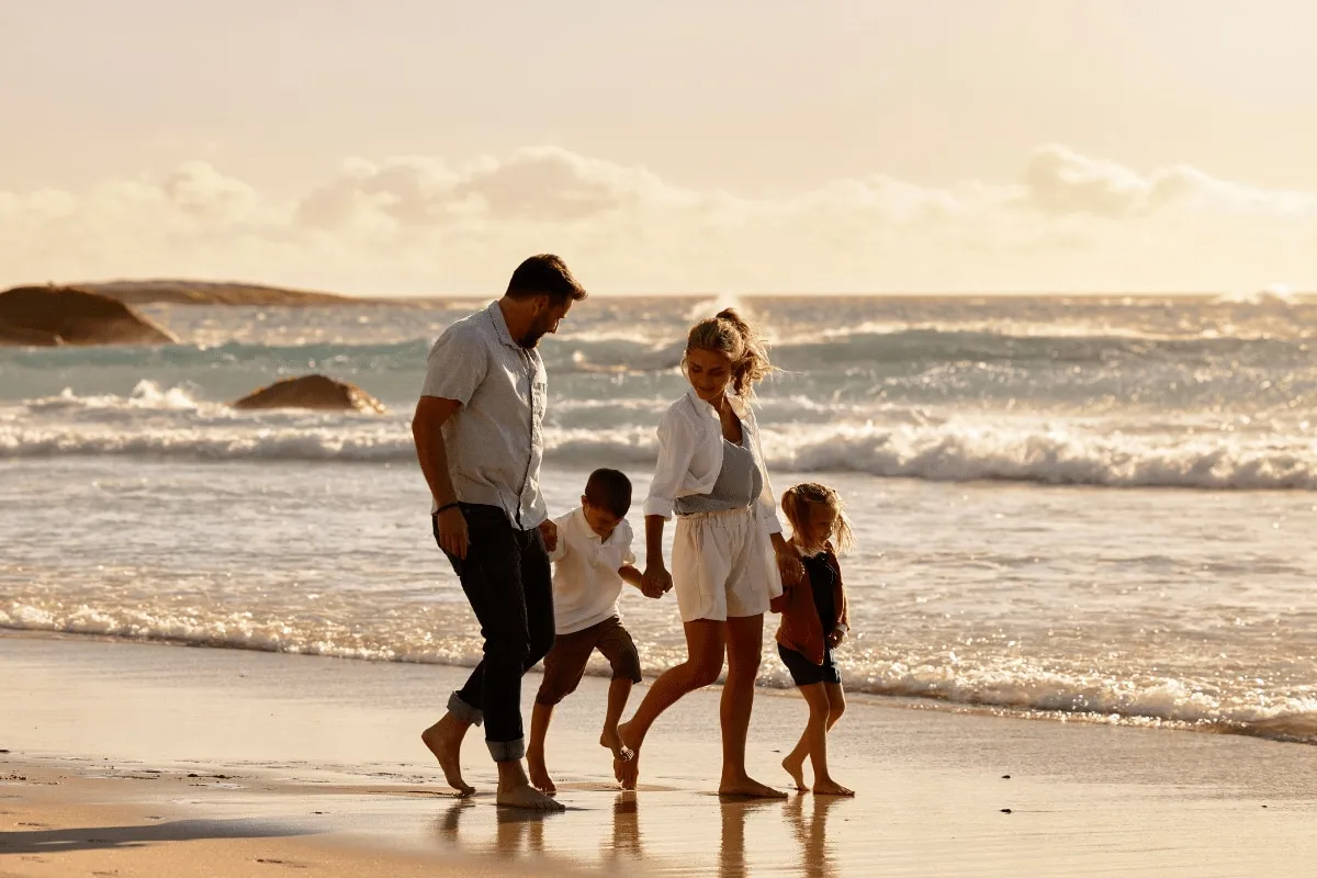 Rodzina spaceruje brzegiem morza, szukając pomysłów, gdzie nad morze z dziećmi tanio. Słońce zachodzi, tworząc złocistą poświatę.