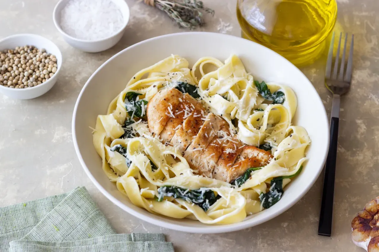 Pyszny obiad: tagliatelle z kurczakiem i szpinakiem w kremowym sosie, posypane parmezanem. Idealne danie na co pysznego na obiad.