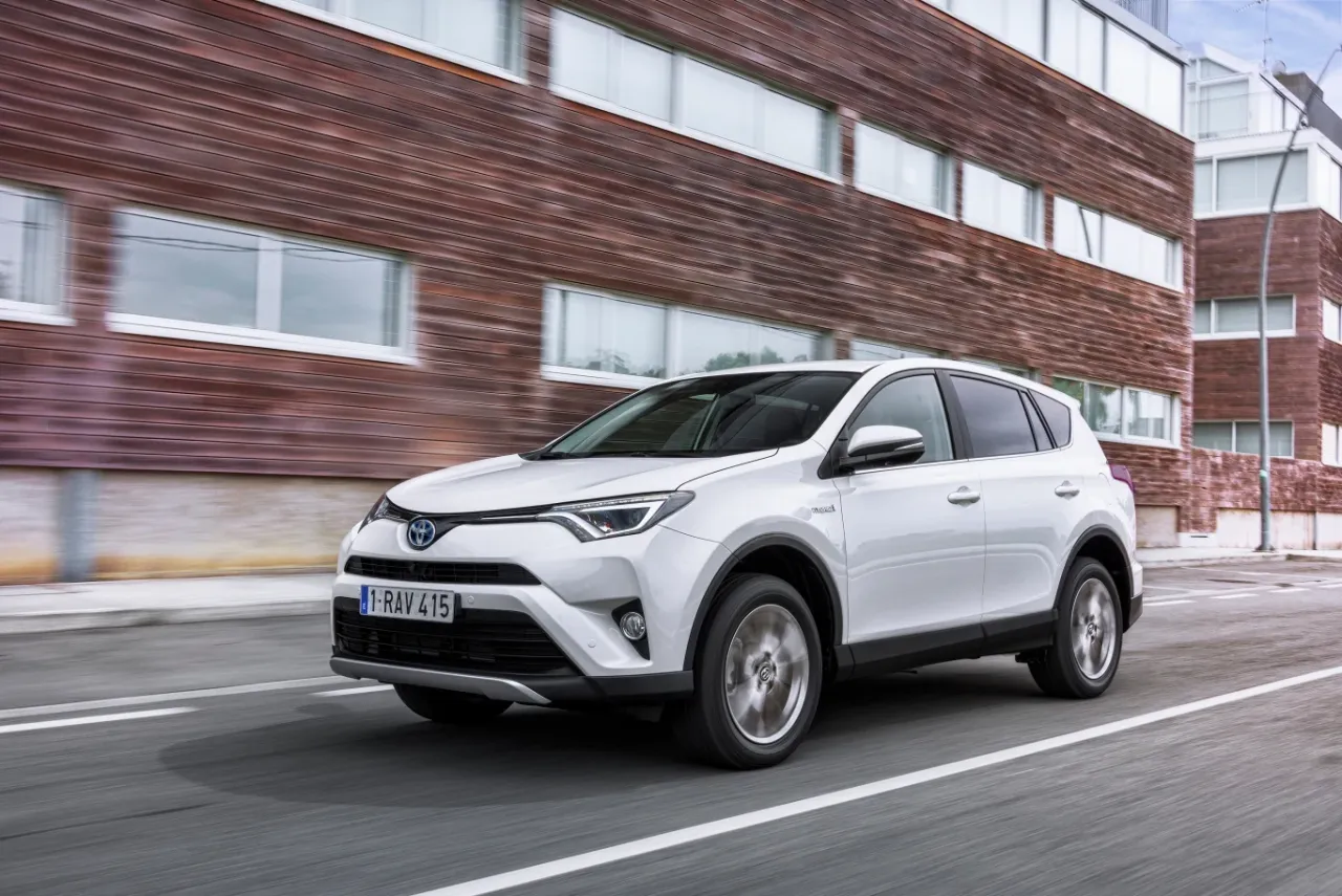 Biała Toyota RAV4 Hybrid jedzie ulicą. Zastanawiasz się, ile kosztuje Toyota? Ten model to świetny wyb&oacute;r.
