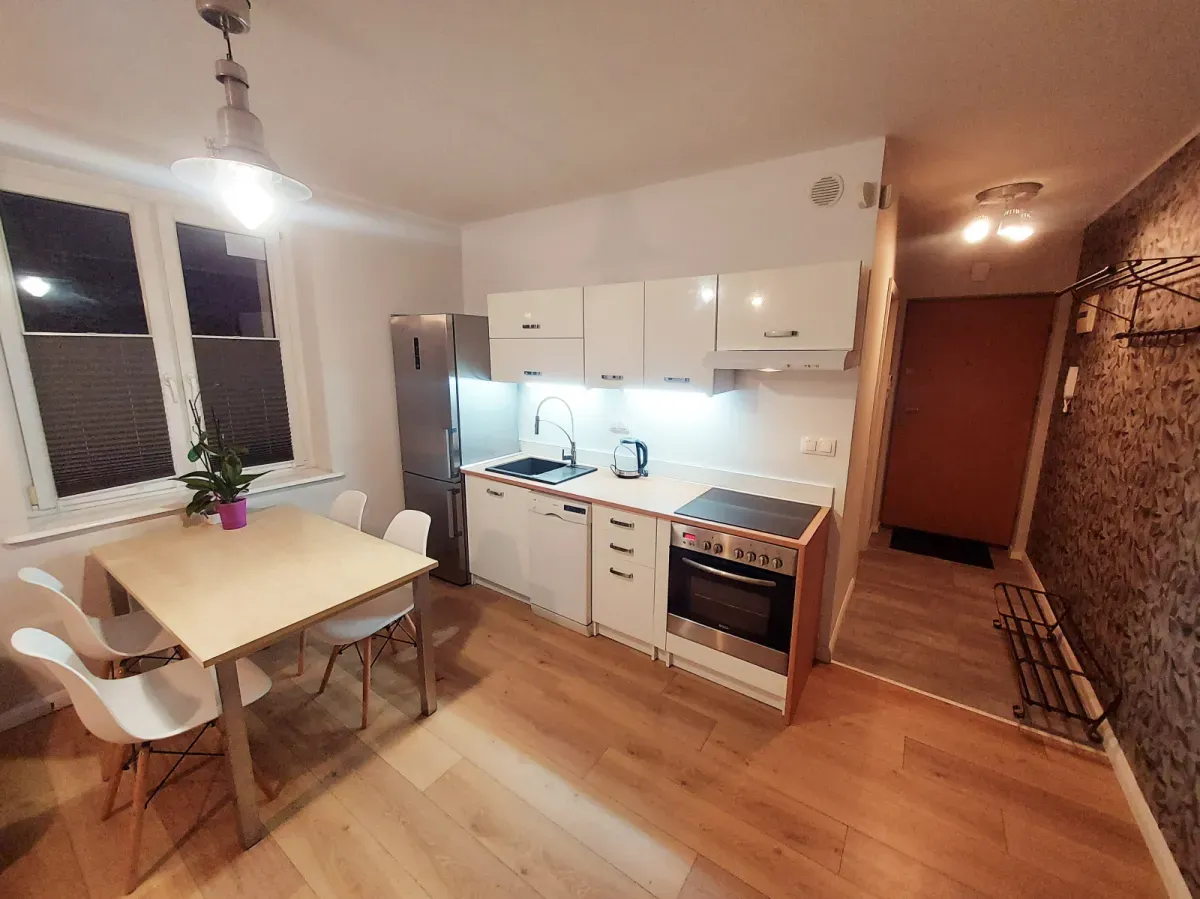 Nowoczesna kuchnia z lodówką, płytą grzewczą i zmywarką. Stół z krzesłami. To wszystko, co potrzebne, by poczuć się jak w domu, nawet gdy zastanawiasz się, co to jest odstępne za mieszkanie.