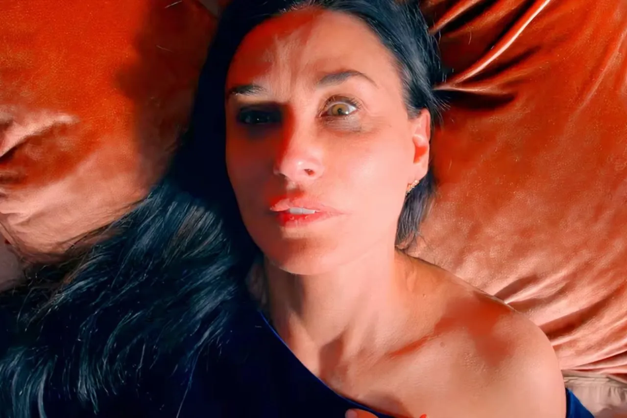 Kobieta leży na aksamitnej poduszce. Jej twarz jest blisko kamery, a oczy szeroko otwarte. Film