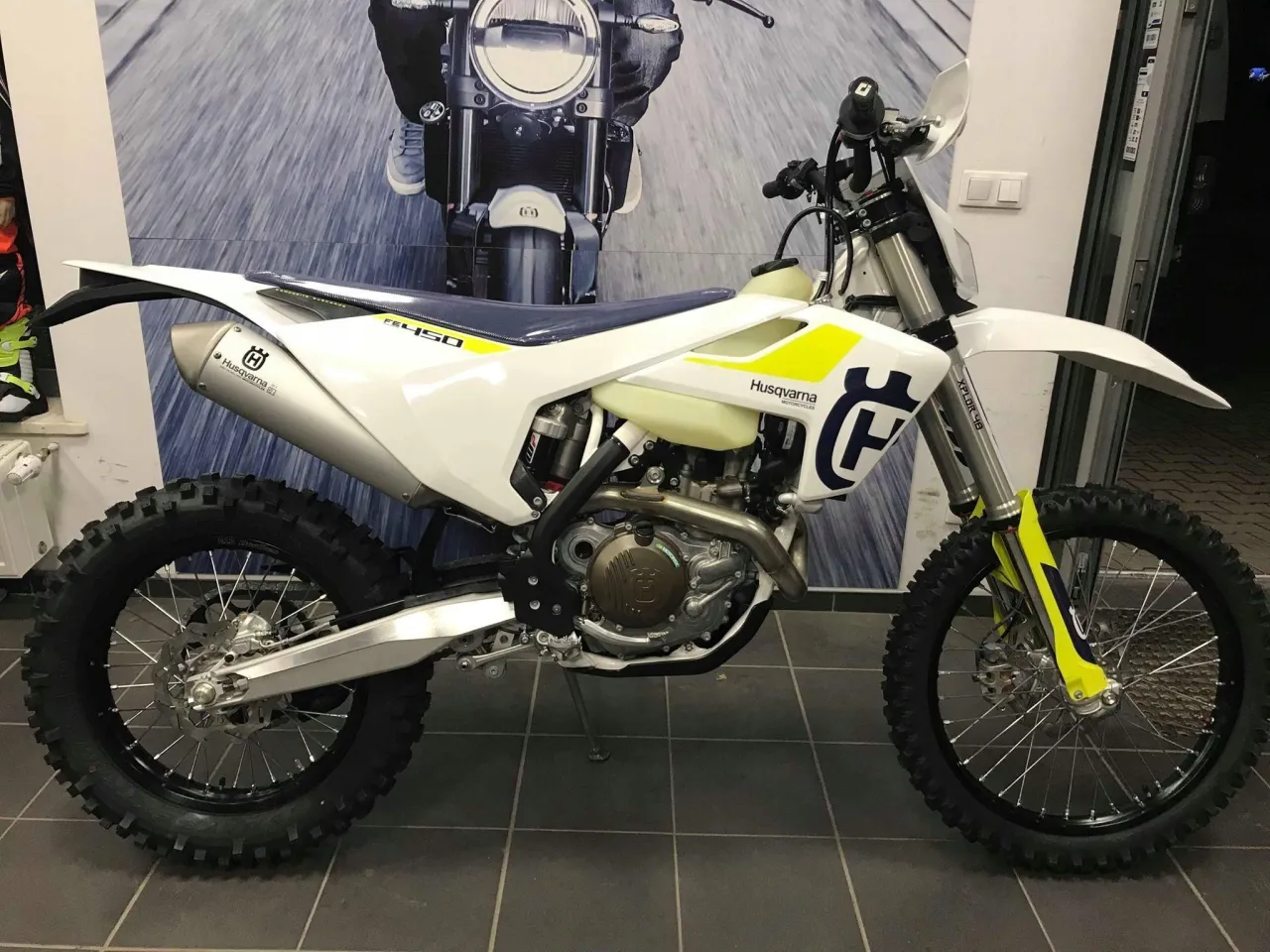 Biały motocykl Husqvarna 450 FE z ż&oacute;łtymi akcentami, gotowy do jazdy terenowej.