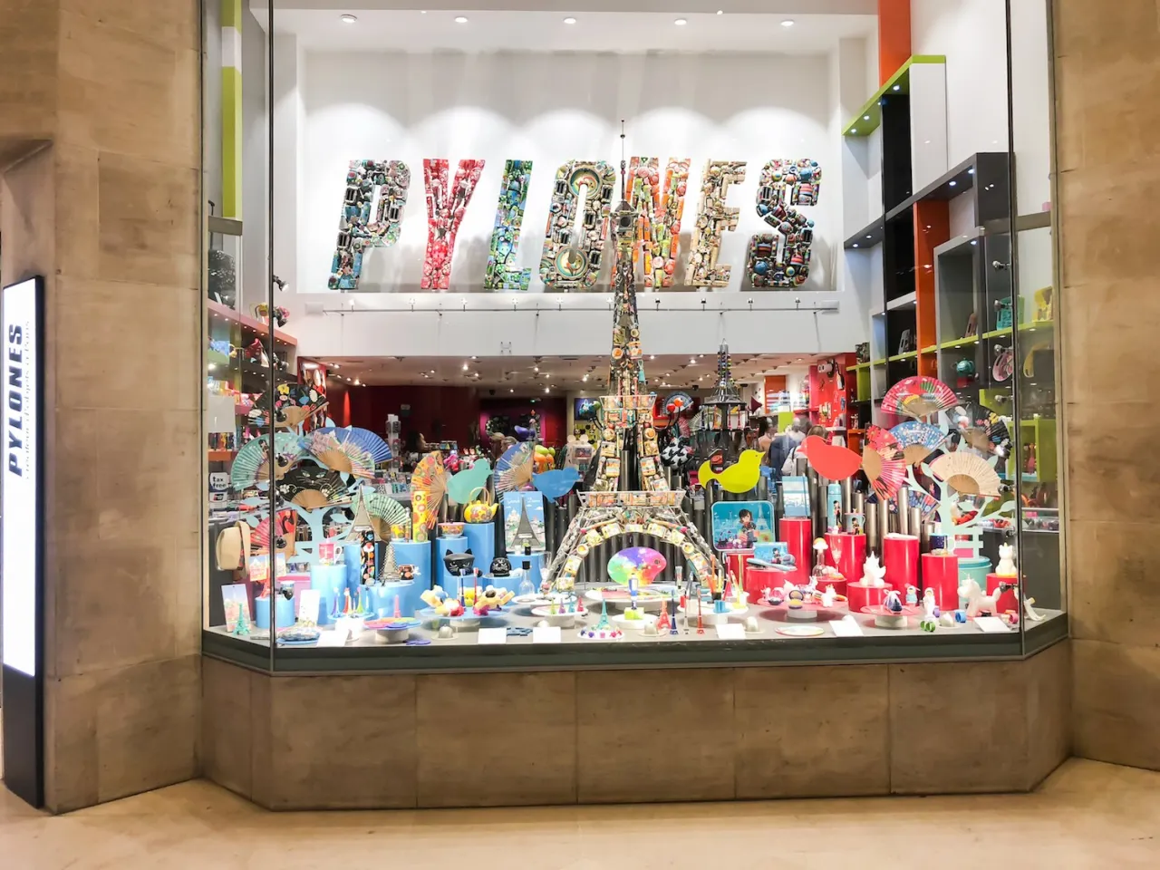 Kolorowa witryna sklepu PYLONES w Paryżu, pełna pamiątek i gadżetów. Idealne miejsce, by dowiedzieć się, co kupić w Paryżu.