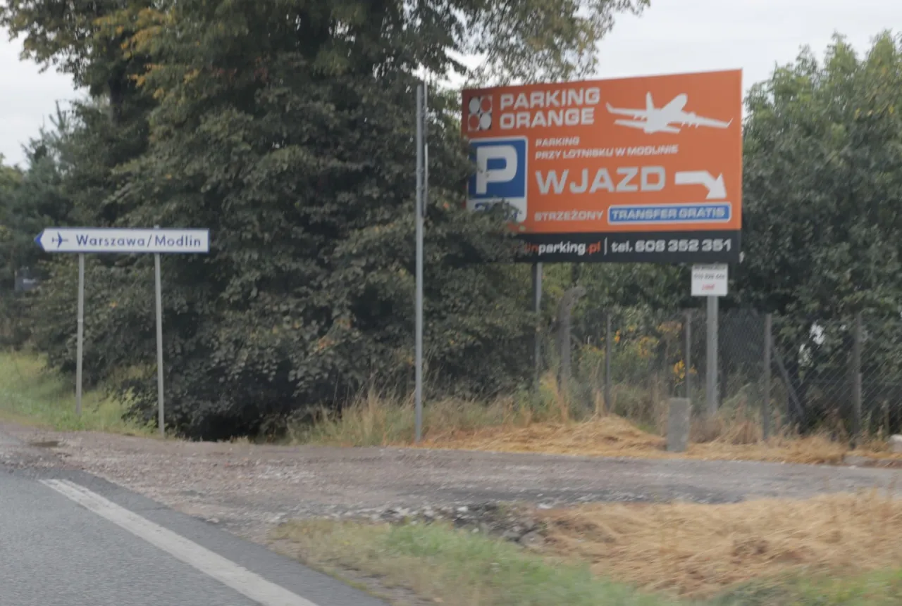 Znak informuje o parkingu przy lotnisku w Modlinie. Sprawdź, ile kosztuje parking na lotnisku w Warszawie, dzwoniąc pod podany numer.