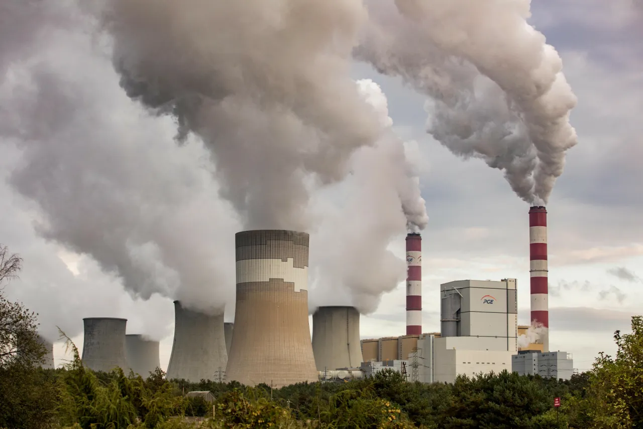 Ogromne chmury pary unoszą się z chłodni kominowych i dwóch czerwono-białych kominów elektrowni Bełchatów, pokazując, ile prądu produkuje elektrownia Bełchatów.