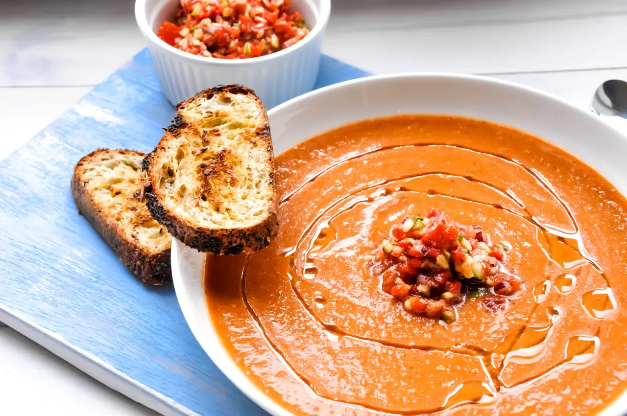 Chłodnik z pomidorów, podany z chrupiącymi grzankami i posiekanymi warzywami, to idealna propozycja na letni posiłek.