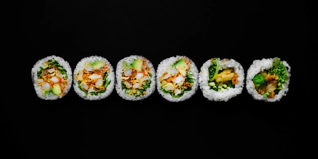 Sześć kawałk&oacute;w sushi: futomaki i uramaki z awokado, kurczakiem i warzywami na czarnym tle.