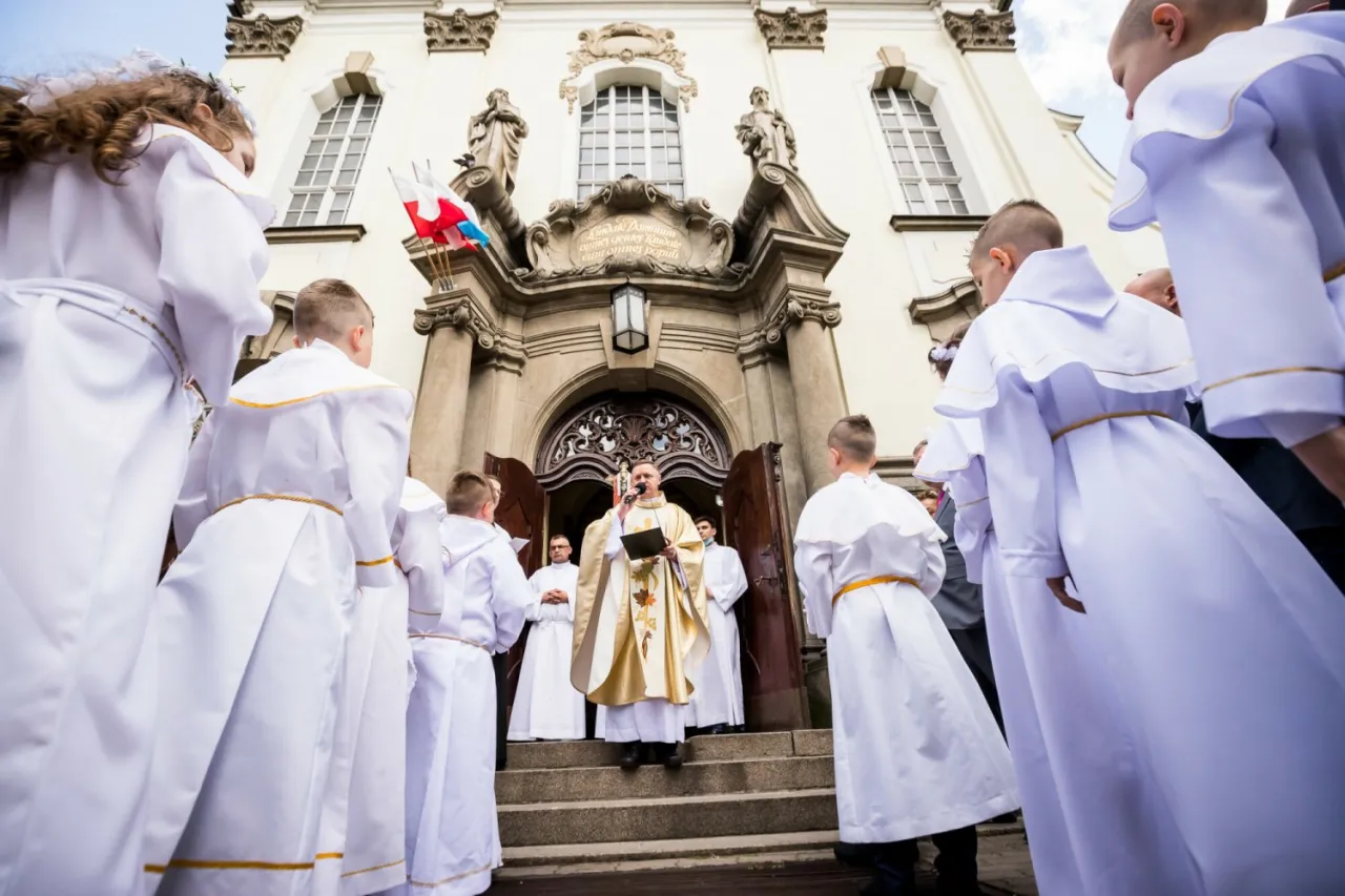 Dziecko w stroju komunijnym z hostią w dłoni