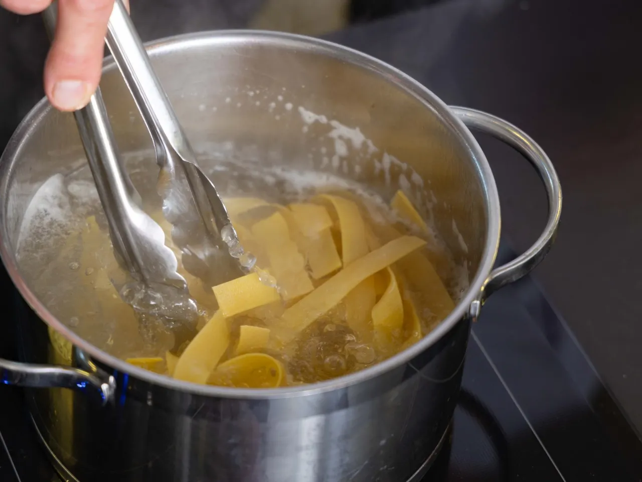 Szczypce wyjmują szeroki makaron z wrzącej wody. Klucz do sukcesu: jak gotować makaron al dente.