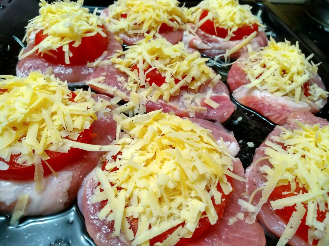 Mięso na obiad: plastry schabu z pomidorami i startym żółtym serem, gotowe do pieczenia.