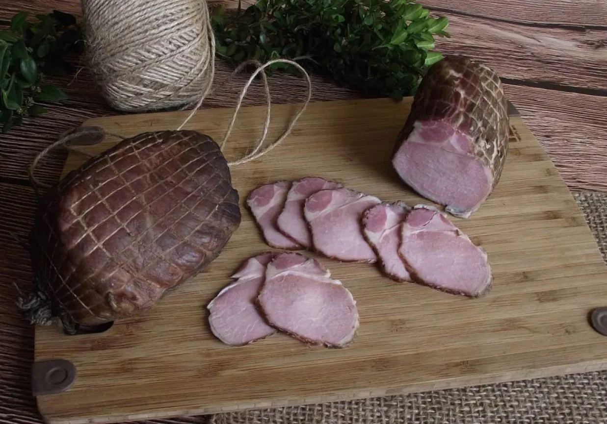 Jak zrobić soczysty schab wędzony? Na desce leżą dwa wędzone kawałki schabu, jeden w całości, drugi pokrojony w plastry.